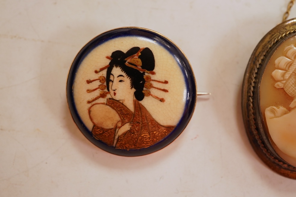 A Satsuma brooch, set with a circular Satsuma plaque depicting an oiran with gilded hair ornaments, mounted in 9ct gold, 3.3cm diameter, British hallmarks; together with an oval shell cameo brooch depicting a classical w